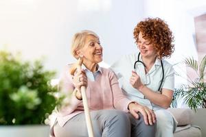 amichevole relazione fra sorridente badante nel uniforme e contento anziano donna. supporto giovane infermiera guardare a anziano donna. giovane cura bello badante e contento reparto foto