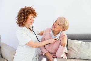 Salute visitatore e un' anziano donna durante casa visitare. giovane femmina medico l'esame anziano paziente. giovane donna medico indossare bianca cappotto l'esame anziano donna. foto