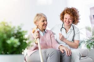 amichevole relazione fra sorridente badante nel uniforme e contento anziano donna. supporto giovane infermiera guardare a anziano donna. giovane cura bello badante e contento reparto foto