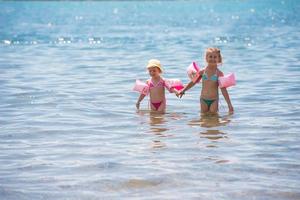 poco ragazze con nuoto bracciali giocando nel superficiale acqua foto
