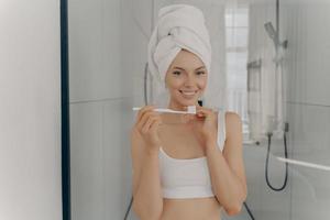 felice bella signora con un sano sorriso perfetto lavarsi i denti mentre si è in piedi in bagno foto