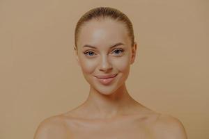 Ritratto di bellezza di una donna affascinante con una pelle sana e luminosa in posa seminuda contro il muro beige foto