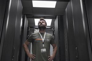ritratto di maschio tecnico o Rete amministratore in piedi coraggioso come un' eroe con braccia attraversato nel dati centro server camera. foto