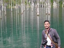 uomo in piedi nel davanti di spoglio tronchi di alberi nel lago kaindy nel Kazakistan foto