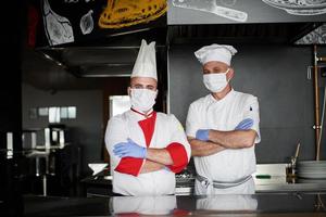 gruppo chef in piedi insieme nel il cucina a ristorante indossare protettivo medico maschera e guanti nel coronavirus nuovo normale concetto foto