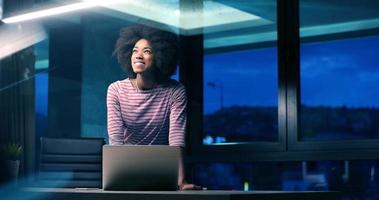 nero donna d'affari utilizzando un' il computer portatile nel notte avviare ufficio foto