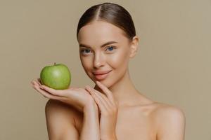 foto di A petto nudo brunetta giovane donna con pettinato capelli detiene fresco verde Mela usi naturale cosmetico ha spoglio le spalle isolato al di sopra di Marrone sfondo. persone cosmetologia corpo cura concetto