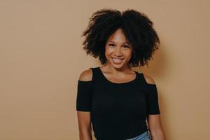 donna afro americana sorridente con i capelli ricci in piedi su sfondo beige foto