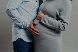 incinta moglie indossa vestito pose vicino marito chi tocchi sua grande gonfiarsi. futuro madre e padre aspettare per nuovo membro di famiglia. paternità concetto foto