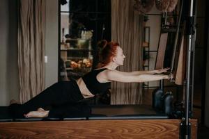 in forma giovane pilates istruttore allungamento braccia su cadillac riformatore foto