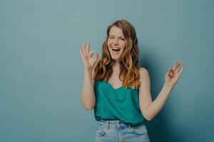 affascinante ragazza divertente mostra segno giusto con le mani, strizzando l'occhio e guardando la fotocamera con un grande sorriso foto