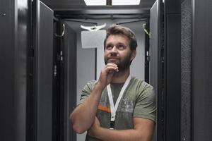 ritratto di maschio tecnico o Rete amministratore in piedi coraggioso come un' eroe con braccia attraversato nel dati centro server camera. foto