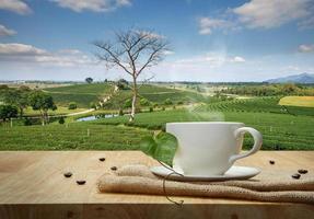 caffè tazza con tela di sacco su il di legno tavolo e il piantagioni sfondo foto