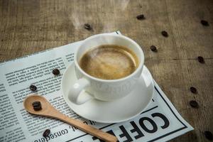 bianca tazza di caffè espresso con giornale su il di legno tavolo nel il mattina foto