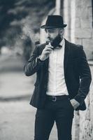un' ricco uomo con un' barba fuma elettronico sigaretta foto