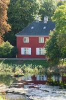 il elementi di un idilliaco estate scena. un' rosso Casa, un' stagno, e luce del sole. foto