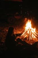 donna seduta e ottenere caldo vicino il falò nel il notte foresta. foto