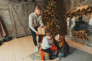 giovane caucasico famiglia mamma papà figlio vicino camino Natale albero foto