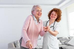 sorridente infermiera porzione anziano signora per camminare in giro il assistenza infermieristica casa. ritratto di contento femmina badante e anziano donna a piedi insieme a casa. professionale badante assunzione cura di anziano donna. foto