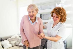 sorridente infermiera porzione anziano signora per camminare in giro il assistenza infermieristica casa. ritratto di contento femmina badante e anziano donna a piedi insieme a casa. professionale badante assunzione cura di anziano donna. foto