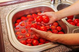 un' donna di mani lavare pomodori sotto in esecuzione acqua nel il cucina lavello. foto