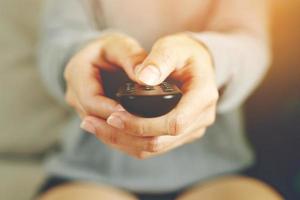 vicino su televisione a distanza controllo nel casuale uomo mano hold puntamento per tv impostato e svolta esso su o spento. Selezionare canale Guardando calcio gioco su tv il suo a casa nel il vivente camera relax. foto