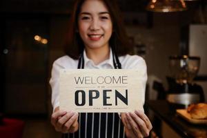 avvicinamento di un' bellissimo asiatico donna Tenere un' cartello per Aperto un' caffè negozio. concettuale imprenditori, pmi imprese, piccolo cibo servizio ristoranti. foto