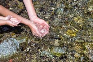 femmina mani notizia in anticipo su fresco acqua nel nel un' montagna ruscello foto