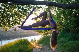 un' giovane ginnasta è impegnato nel aereo yoga nel natura nel il parco, utilizzando un' combinazione di tradizionale yoga pose, pilates e dolce danza foto