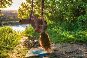 un' giovane ginnasta è impegnato nel aereo yoga nel natura nel il parco, utilizzando un' combinazione di tradizionale yoga pose, pilates e dolce danza foto