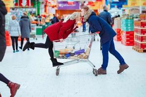 giovane bello tipo cavalcate un' ragazza nel un' supermercato nel un' carrello foto