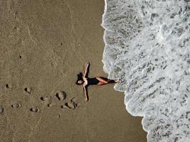 aereo superiore Visualizza giovane donna dire bugie su il sabbia spiaggia e onde foto