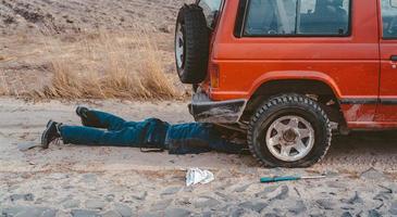 uomo bugie sotto un' 4x4 auto su un' sporco strada foto