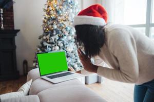 femmina indossare Santa cappello mentre A proposito di con in linea amico su il computer portatile foto