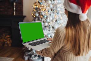 femmina indossare Santa cappello mentre A proposito di con in linea amico su il computer portatile foto