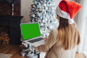 femmina indossare Santa cappello mentre A proposito di con in linea amico su il computer portatile foto