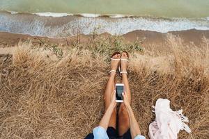 bellissimo giovane ragazza seduta e Tenere un' smartphone nel sua mani, superiore Visualizza foto