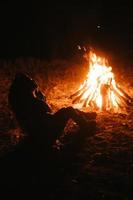 donna seduta e ottenere caldo vicino il falò nel il notte foresta. foto