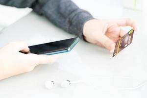 donna seduta e utilizzando smartphone per in linea shopping con credito carta su ponte nel casa ufficio foto