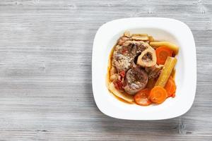 italiano piatto osso buco nel bianca piatto su grigio tavola foto