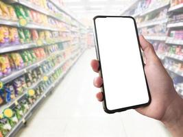 inteligente shopping concetto mobile Telefono nel mano nel davanti di merce scaffali nel supermercato e drogheria negozio. vuoto bianca schermo modello per il tuo proprio creatività. foto