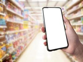 inteligente shopping concetto mobile Telefono nel mano nel davanti di merce scaffali nel supermercato e drogheria negozio. vuoto bianca schermo modello per il tuo proprio creatività. foto