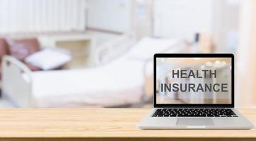 computer portatile su un tavolo di legno con testo di assicurazione sanitaria sullo schermo con sfocatura dello sfondo della stanza d'ospedale concetto sanitario foto