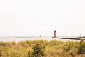 faro a fine di molo su un' nuvoloso ventoso giorno su lago Michigan. lungo molo. asciutto erbe in crescita nel il sabbia colline. rosso e verde boe marcatura il porto ingresso. foto