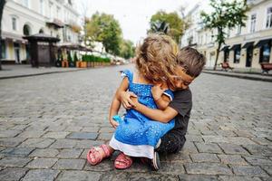 poco ragazzo e ragazza siamo seduta su il strada foto