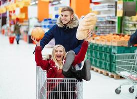 giovane bello tipo cavalcate un' ragazza nel un' supermercato nel un' carrello foto