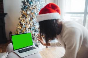 femmina indossare Santa cappello mentre A proposito di con in linea amico su il computer portatile foto