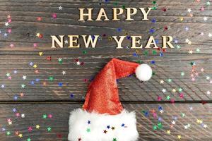 contento nuovo anno 2023 di legno lettere citazione con rosso scintillante Santa cappello su di legno tavolo con luccichio. festivo saluto carta per un' nuovo anno celebrazione foto