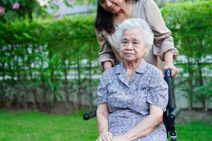 il caregiver aiuta il paziente con disabilità della donna anziana asiatica seduto su una sedia a rotelle nel parco, concetto medico. foto