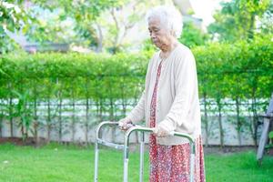 camminata del paziente di disabilità della donna anziana asiatica con il deambulatore nel parco, concetto medico. foto